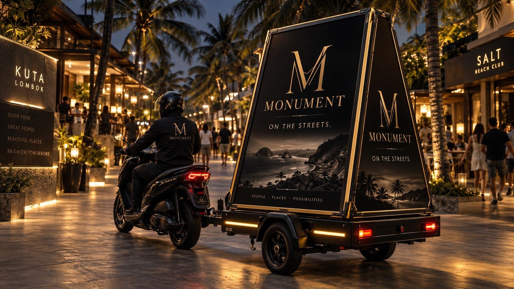 A MONUMENT Mobile scooter towing an illuminated billboard trailer through a busy Kuta Lombok street at night